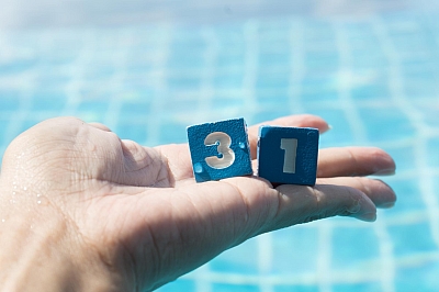 Blaue Würfel auf offener Handfläche vor einem Schwimmbecken